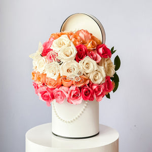 A stunning floral arrangement featuring a white pedestal and a mix of pink and orange roses, with green leaves.