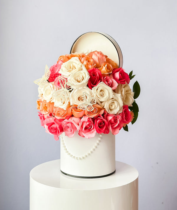A stunning floral arrangement featuring a white pedestal and a mix of pink and orange roses, with green leaves.