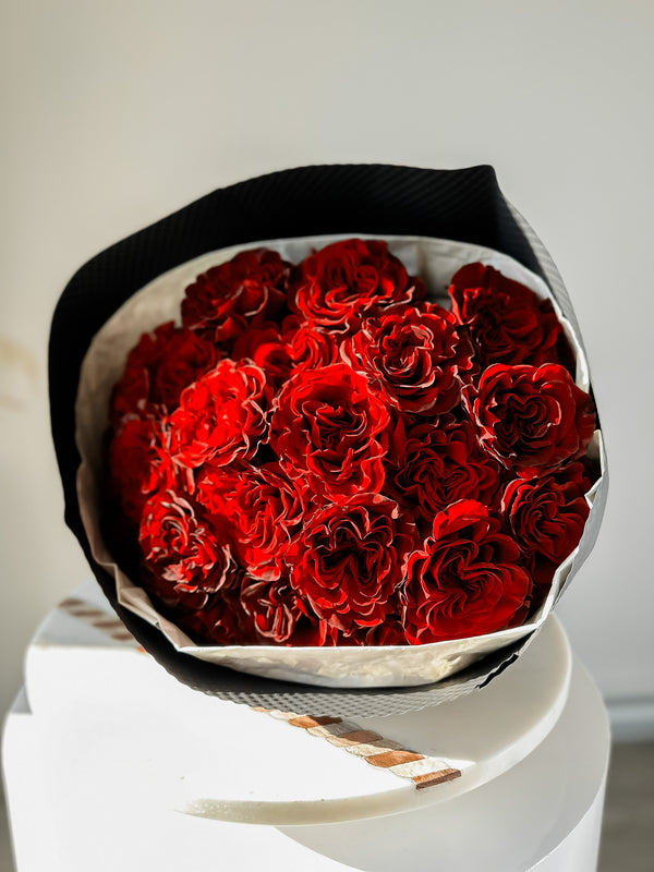 A bouquet of red heart-shaped flowers, with prominent dark red accents on the petals, wrapped in a premium material and tied with an elegant ribbon.