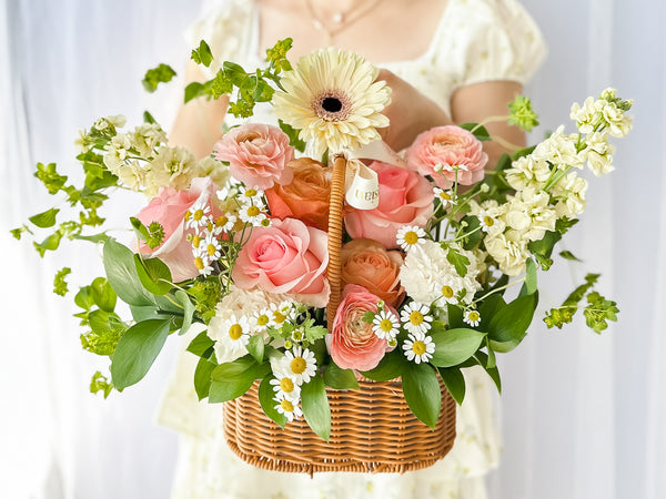 Close-up of a floral arrangement featuring a variety of flowers in pink, yellow, and white, nestled in a wicker basket.