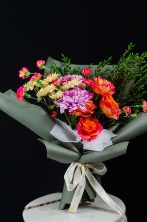 Bouquet of flowers wrapped in green paper with a white ribbon on a black background