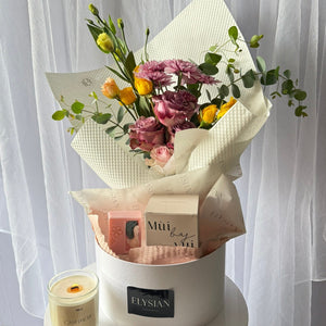 Bouquet of flowers in a white box with a candle on a white surface and white curtain background