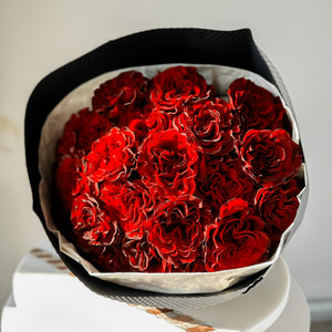A bouquet of red heart-shaped flowers, with prominent dark red accents on the petals, wrapped in a premium material and tied with an elegant ribbon.