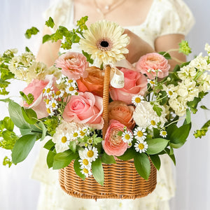 Close-up of a floral arrangement featuring a variety of flowers in pink, yellow, and white, nestled in a wicker basket.