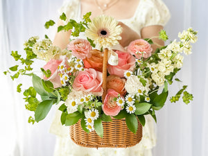 Close-up of a floral arrangement featuring a variety of flowers in pink, yellow, and white, nestled in a wicker basket.