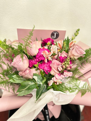 Bouquet of pink and purple flowers with greenery, wrapped in white paper.